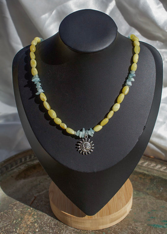 Necklace with yellow beads and a silver sun pendant on a black mannequin bust.